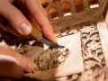 Main tenant, avec un petit couteau, nettoie un meuble ancien orné de motifs floraux complexes.