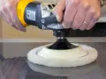 Main d'artisan utilisant une polisseuse pour polir le vernis d'un meuble en bois.