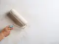 Main d'une personne appliquant une couche de peinture sur un mur déjà peint avec un rouleau.