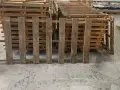 Des planches de bois recycle, issues de palettes, forment une barrière devant d'autres palettes empilées.
