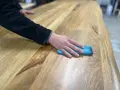Main d'une personne passant un chiffon bleu sur une table en bois, montrant comment nettoyer une table en bois.