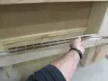 Main tenant une longue charnière piano pour la fixer sur un meuble en bois.