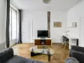 Salon moderne avec parquet en chevrons, canapés gris, bureau et TV. Les murs et le plafond sont peints à l'huile, offrant une finition impeccable.
