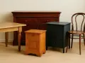Meubles anciens repeints : commode sombre, table en bois clair, chevet orangé et chaise courbée.