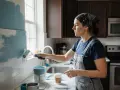 Une femme en salopette repeint sa cuisine avec un rouleau bleu pâle. La transformation de la cuisine repeinte est en cours.