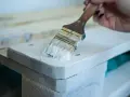 Application de peinture glycéro sur bois brut, sans poncer. La brosse dépose une couche blanche sur la surface.