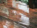Pluie sur un bois brun, saturateur pas sec, créant des reflets et des ronds dans l'eau.