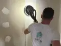 Un ouvrier utilise une ponceuse girafe pour poncer un mur en plâtre, préparant la surface pour la peinture.