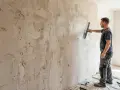 Un ouvrier applique du plâtre sur un mur avec une truelle, prêt à gratter le mur pour une finition lisse.