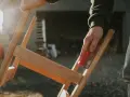 Main d'artisan ponçant un meuble en bois, préparant la surface pour enlever peinture sur bois acétone. Poussière de bois en suspension.