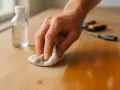 Main d'une personne utilisant un chiffon pour enlever le vernis bois naturellement. Une bouteille de liquide est à côté.