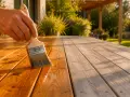 Main d'une personne appliquant un saturateur sur une terrasse en bois. Aide à choisir quel saturateur choisir pour protéger et embellir le bois.