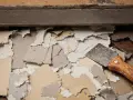 Un grattoir à peinture, avec son manche en bois, est posé sur des morceaux de **peinture qui s'enlève facilement**, révélant le support en dessous.