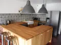 Cuisine moderne avec îlot central en bois, carrelage mural graphique et tabourets industriels. On dirait qu'on a réussi à faire une cuisine avec des vieux meubles revisités.