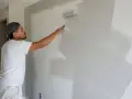 Un peintre applique une couche de peinture grise sur un mur. La question est : peut on enduire sur de la peinture ?
