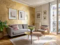 Un salon élégant avec un mur texturé doré, un canapé gris, un fauteuil, une table basse et des tableaux. Une idée pour comment faire du doré avec de la peinture.