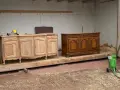 Deux commodes en bois, l'une brute et l'autre vernie, témoignent d'une **réparation meuble en bois**. Un équipement de sablage est prêt à l'emploi.