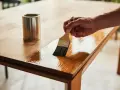 Main d'un artisan appliquant du vernis pour customiser et relooker une table en bois.