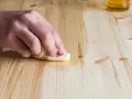 Main d'une personne nettoyant une table en bois avec du vinaigre blanc et un chiffon.