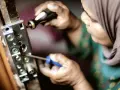 Une personne en hijab utilise un tournevis pour enlever vieux gonds d'une porte en bois.