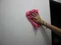 Main tenant une lingette rose pour nettoyer un mur. Une astuce pour savoir comment enlever de la colle forte sur un mur.