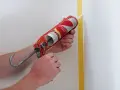 Application de silicone avec un pistolet pour une finition parfaite. Le joint de silicone est appliqué le long d'un coin de mur masqué par du ruban de peintre.