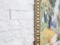 Un mur en pierre peint en blanc sert de toile de fond à un tableau aux couleurs vives, encadré d'or.