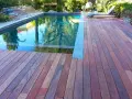 Terrasse en padouk vieilissant, reflétant les arbres dans la piscine. Un transat attend au soleil.