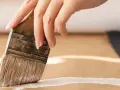 Main d'une personne appliquant une couche de primaire sur du mdf avec un pinceau.