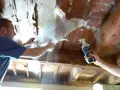 Un homme utilise un produit pour nettoyer des poutres en bois, retirant une vieille couche de revêtement.