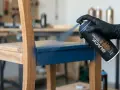 Main d'une personne portant un gant noir en train de peindre un meuble en bois avec une bombe de peinture bleue.