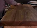 Un artisan polit un meuble en bois de noyer, révélant la beauté du grain. L'essence de térébenthine est utilisée pour faire ressortir la richesse du bois.