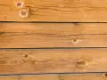 Planches de bois brun clair, traitées avec une lasure bois autoclave, révélant des nœuds et des veines naturelles.