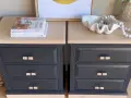 Deux commodes relookées noir et bois, avec des poignées en rotin, des livres et une coquille décorative.