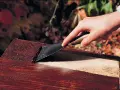 Main d'une personne utilisant un grattoir pour enlever de la peinture d'un meuble en bois, comme avec un décapant peinture bois fait maison.