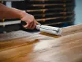 Main d'artisan appliquant une couche de vernis pour vitrifier un plan de travail en bois.