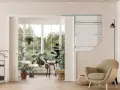 Vue d'un salon lumineux avec une grande baie vitrée donnant sur un jardin luxuriant. Un type de porte coulissante est visible, séparant l'espace intérieur de la véranda.