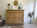 Buffet en bois clair, prêt pour sa restauration. Deux tiroirs et deux portes ornées de moulures. Décoration champêtre avec des vases anciens et des herbes sèches.