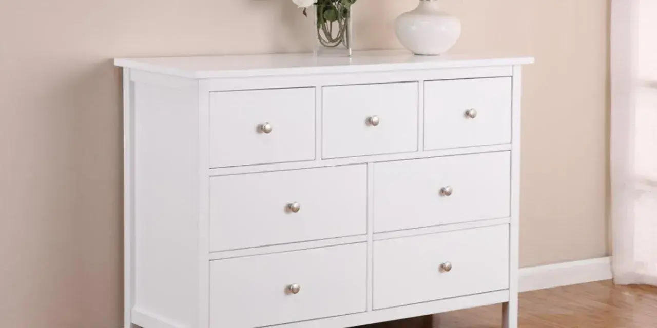 Commode blanche 3 tiroirs, prête à être relookée. Un vase de fleurs et une lampe complètent la scène.