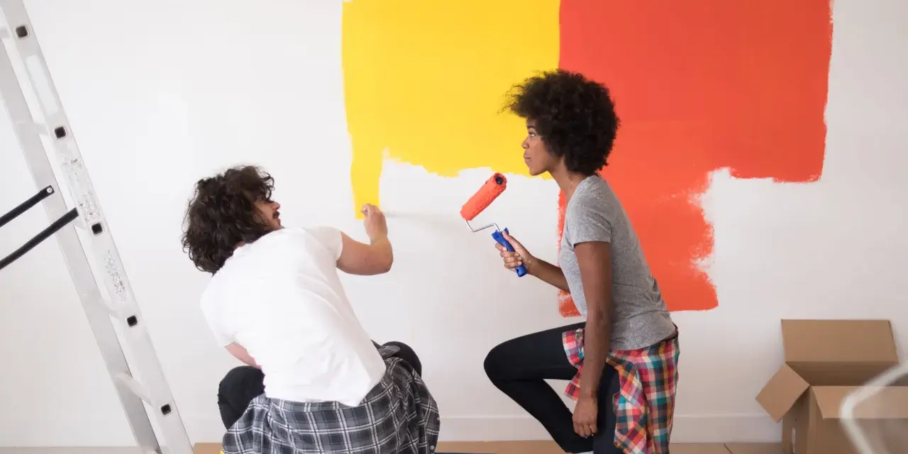 Un couple peint un mur en jaune et orange. Ils utilisent des rouleaux pour nettoyer peinture glycero. Une échelle est à gauche.