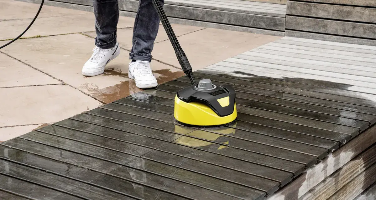Nettoyage d'une terrasse en bois avec un karcher. L'appareil jaune et noir nettoie le bois sombre, laissant une surface plus claire et humide.