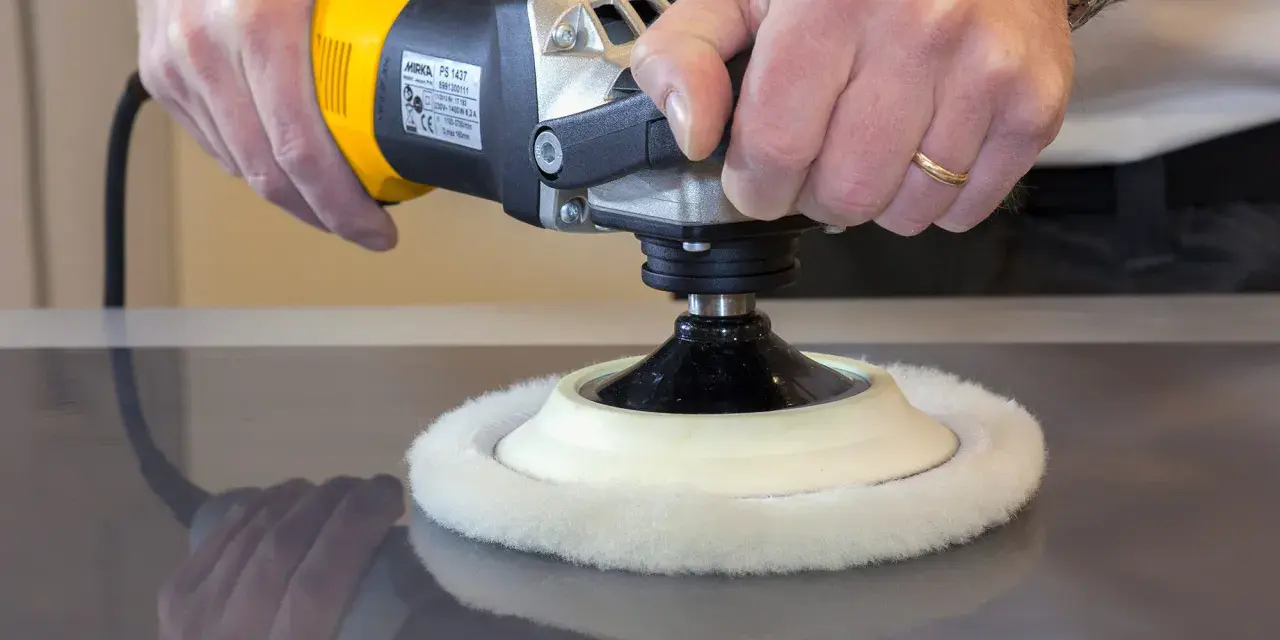 Main d'artisan utilisant une polisseuse pour polir le vernis d'un meuble en bois.