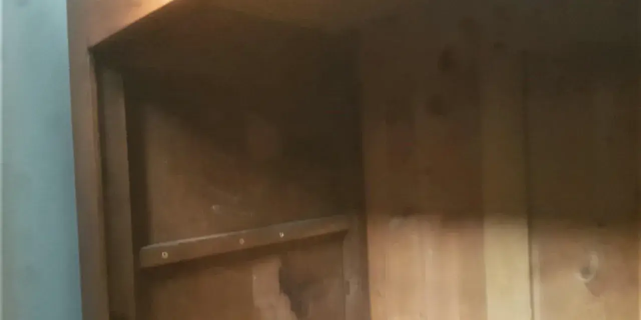 Intérieur d'une armoire ancienne en bois, prête à démonter. Les étagères sont visibles, ainsi que les marques du temps.