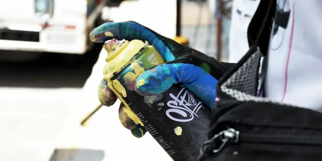 Main tenant une bombe de peinture jaune, un gant coloré montre comment enlever de la bombe de peinture.