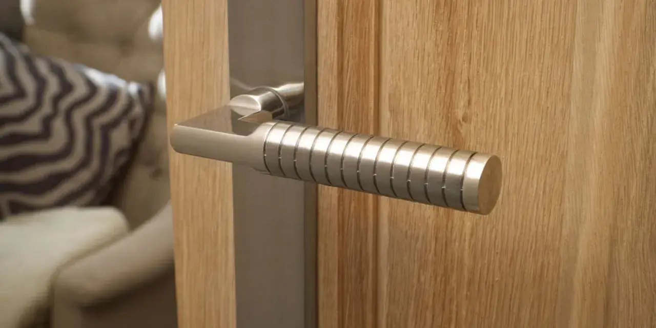 Composition d'une poignée de porte moderne en métal brossé sur une porte en bois clair. Le manche est strié pour une meilleure prise.