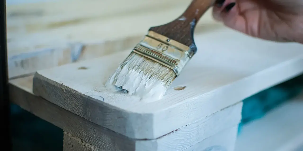 Application de peinture glycéro sur bois brut, sans poncer. La brosse dépose une couche blanche sur la surface.