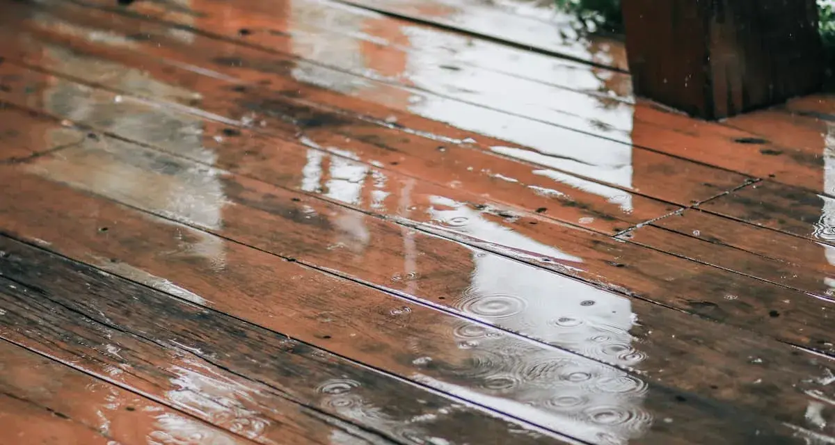Pluie sur un bois brun, saturateur pas sec, créant des reflets et des ronds dans l'eau.