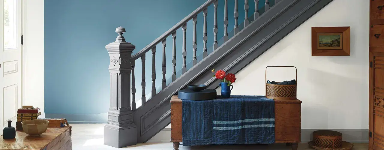 Escalier gris anthracite, une couleur escalier tendance, avec un mur bleu doux. Un bouquet de fleurs rouges sur un coffre en bois.
