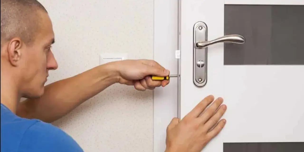 Un homme utilise un tournevis pour installer une serrure sur une porte de chambre.