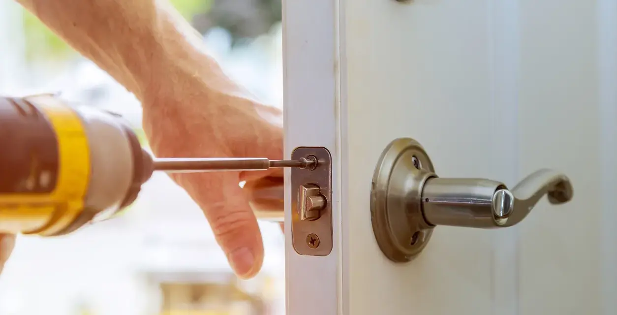 Main tenant répare une serrure cassée sur une porte fermée. Un tournevis est utilisé pour fixer le mécanisme.